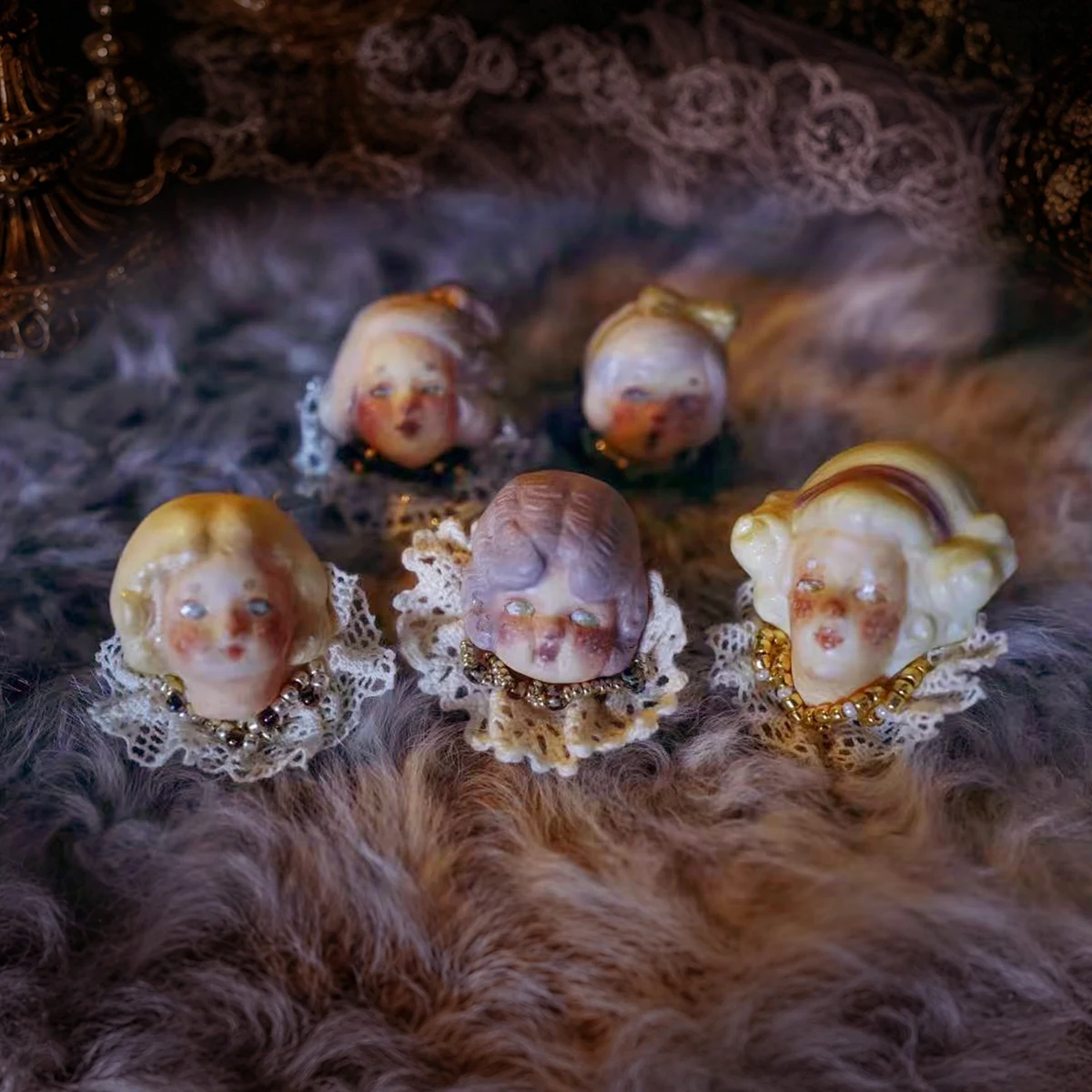 Five Lambwick doll faces with lace collars and jeweled details, nestled in soft plum fabric.