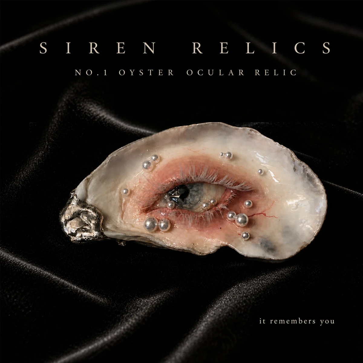 A pearl-adorned oyster shell sculpture with a lifelike eye, resting on black fabric.